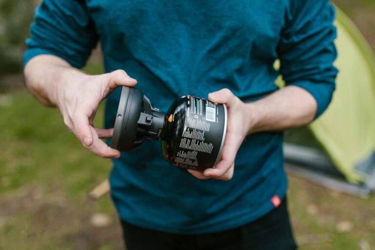A man handling a portable camping stove near a tent in a grassy outdoor area.