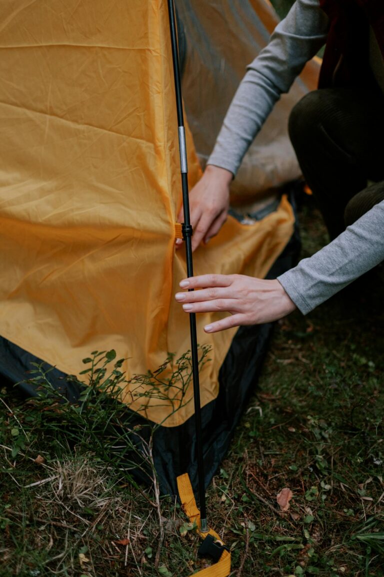 Close-up of a person setting up a tent, focusing on hands and tent pole assembly.