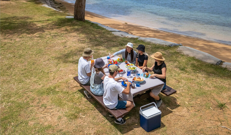 A group of people eating at a picnic table by the water at The Basin campground 768x450