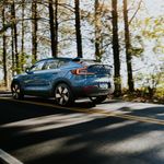 Blue electric car cruising through a scenic forest road during the day, capturing the essence of sustainable travel.